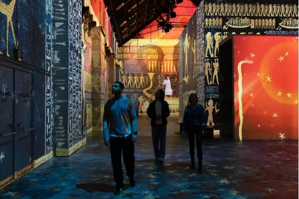 People walking in immersive exhibtition hieroglyphs projected